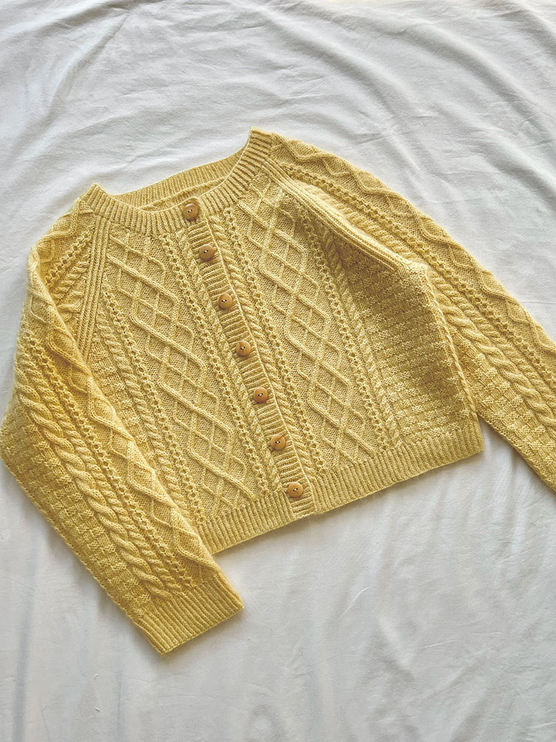 Yellow cable-knit cardigan laid flat, featuring button front and textured sleeves