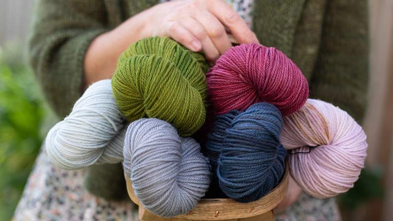 Person holding basket filled with colorful yarn skeins for knitting projects