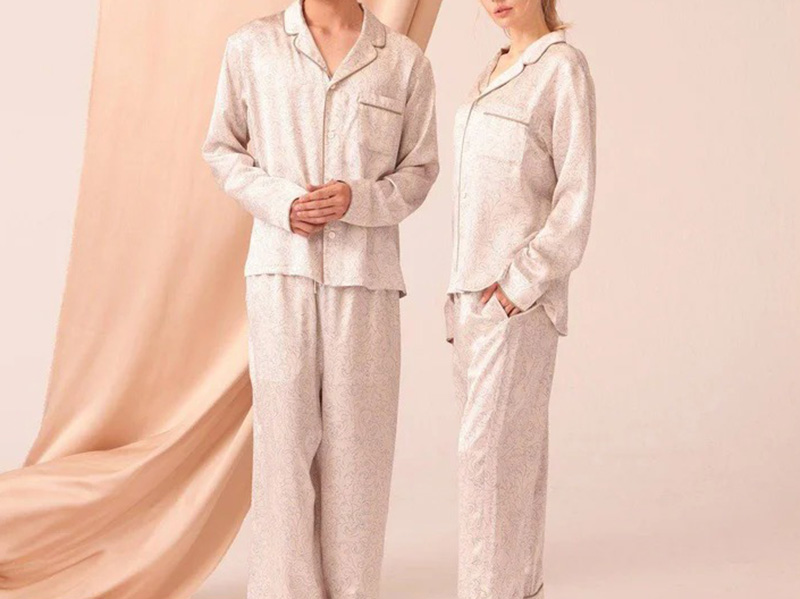 Two models wearing matching light beige patterned pajama sets with button-front tops.