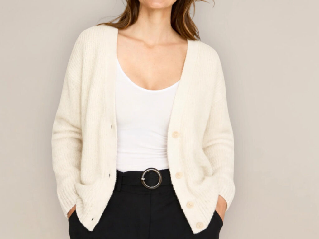 Woman wearing a soft white cardigan over a fitted white top with black trousers.