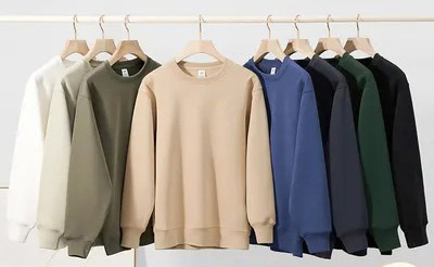 Row of crewneck sweatshirts hanging in white, olive, beige, blue, green, and black.