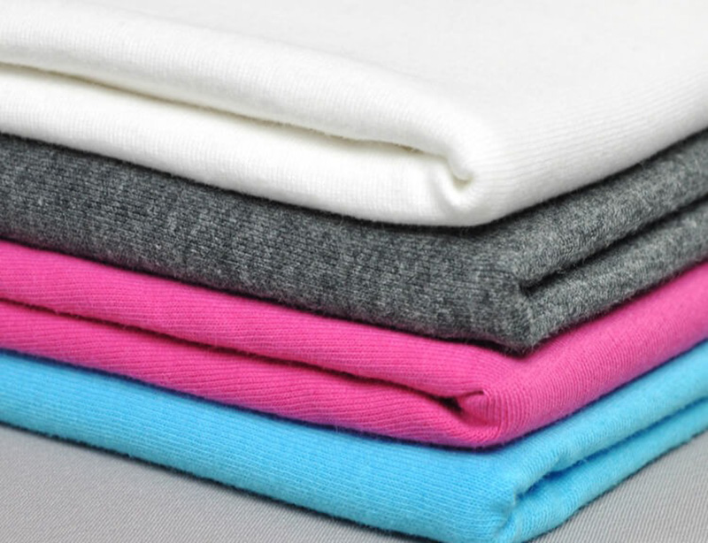 Folded knit fabrics stacked in white, gray, pink, and blue colors.