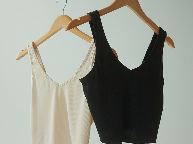 Two ribbed tank tops hanging on wooden hangers in black and cream colors.