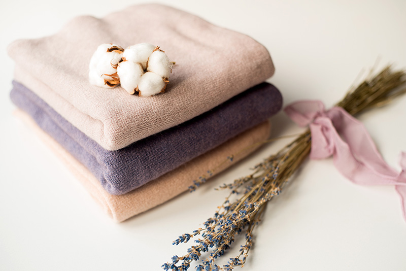 Folded pastel knit fabrics stacked with cotton flower and dried lavender beside them.