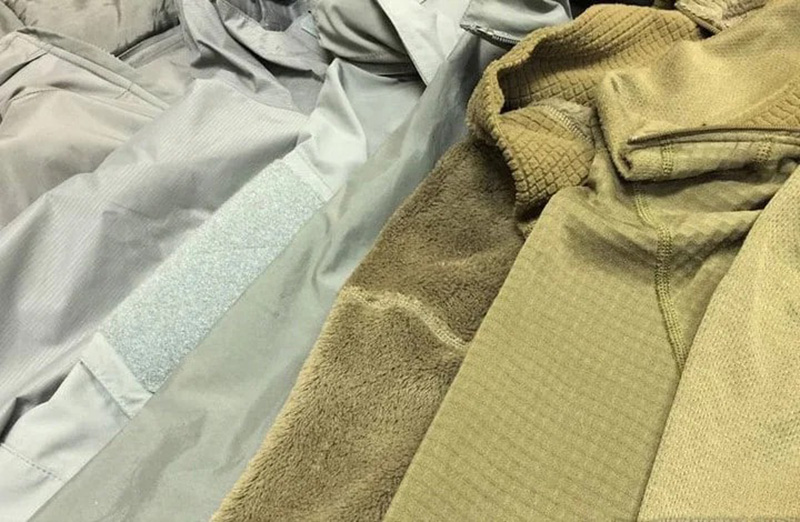 Close-up of folded clothing fabrics in gray and olive tones, showing different textures including fleece and woven materials.