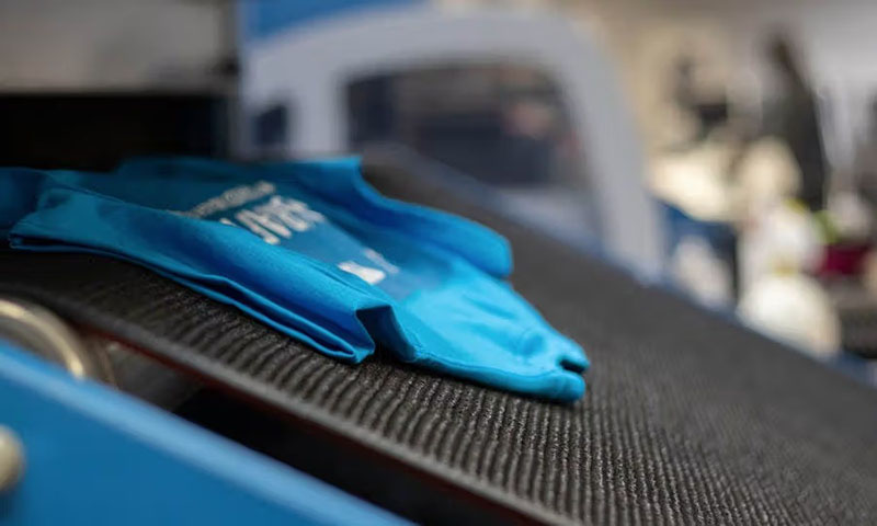 Blue t-shirt moving through automated textile printing conveyor machine system