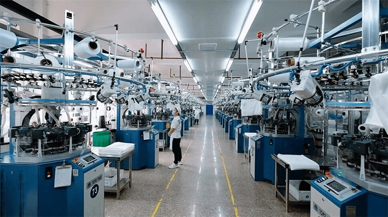 A large industrial textile factory with multiple automated circular knitting machines arranged in rows.
