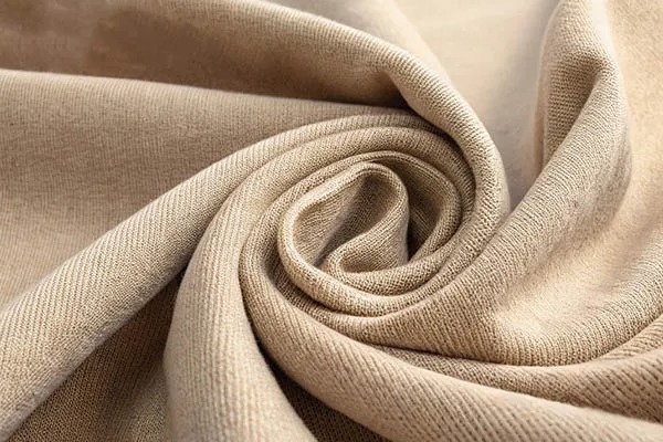 Close-up of beige knit cotton-poly blends fabric twisted into soft folds, showing smooth texture.