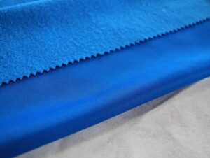 Blue fleece-lined fabric with smooth outer surface and soft brushed interior texture for activewear and winter clothing
