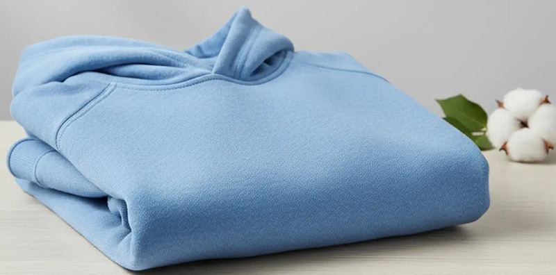 Folded light blue fleece hoodie on table with cotton stems beside it