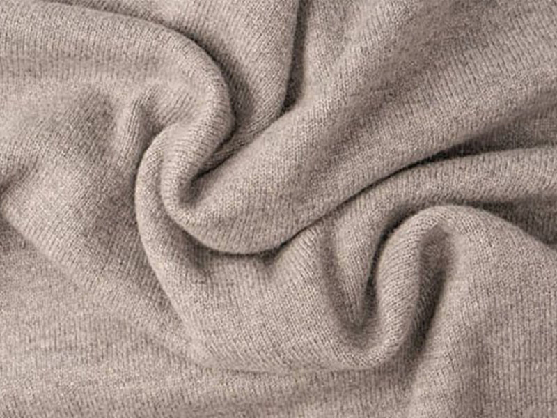 A close-up view of a soft beige fabric with fine texture, gently twisted to show its smooth and cozy appearance.