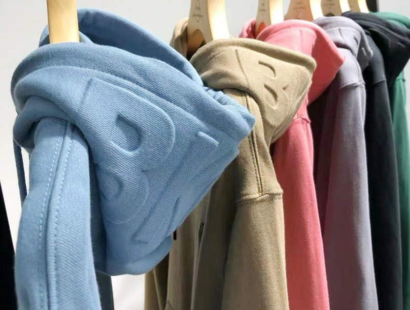 Row of hoodies hanging on wooden hangers in blue, beige, pink, gray, and green colors.