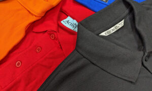 Close-up of folded polo shirts in orange, red, blue, and gray fabrics with visible collars and tags.