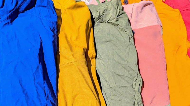 Brightly colored winter jackets laid out side by side in blue, yellow, green, pink, and orange.