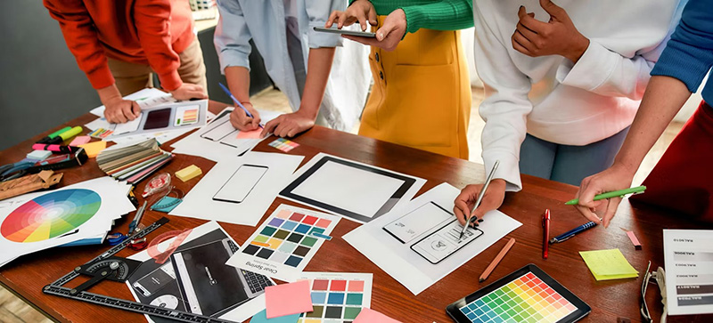 People collaborating at a table with sketches, color palettes, and design tools.