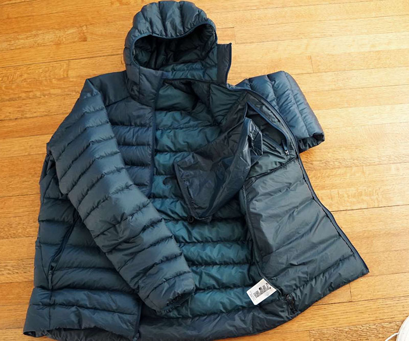 Dark blue hooded down jacket laid flat on a wooden floor, partially unzipped showing inner lining.