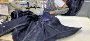 Worker sewing blue denim jeans on industrial machine in garment manufacturing factory setting