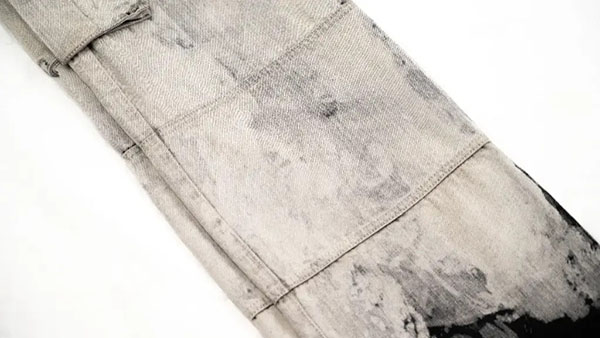 Close-up of washed gray denim with patchwork panels and distressed fade details.