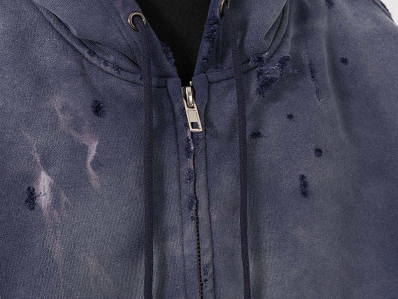 Close-up of distressed navy zip hoodie with faded wash and worn hole details.