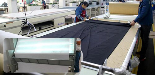 Textile factory workers cutting fabric on industrial production table machinery