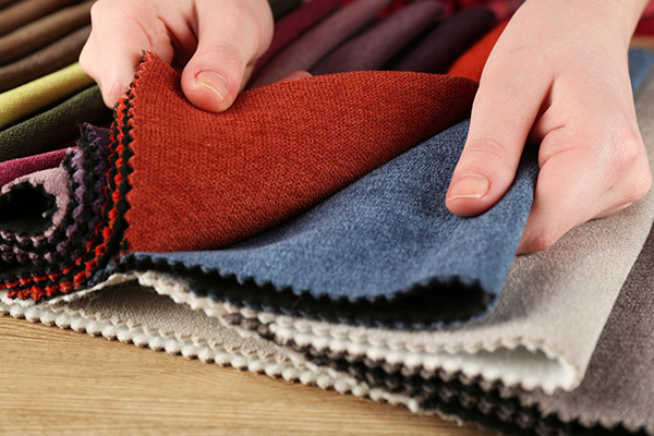 Hands comparing layered fabric swatches in rust, blue, cream, and neutral colors.