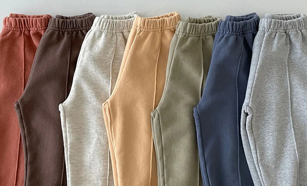 Seven fleece jogger sweatpants in muted shades including rust, brown, cream, tan, sage, blue, and gray.