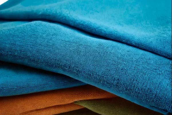 Close-up of folded fabrics in bright blue, orange, and green, showing textured material layers stacked neatly.