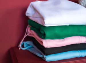 Stack of folded hoodies in white, green, pink, black, and blue casual streetwear colors