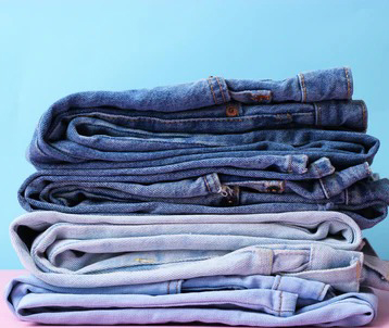 Stack of folded denim jeans in different blue washes on a pastel background.