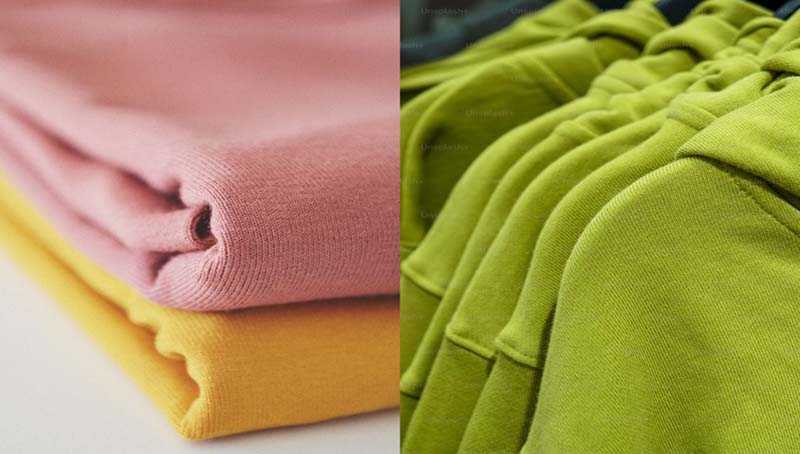 Close-up of folded fabrics in pink and yellow on the left, and a row of green hooded sweatshirts on hangers on the right.