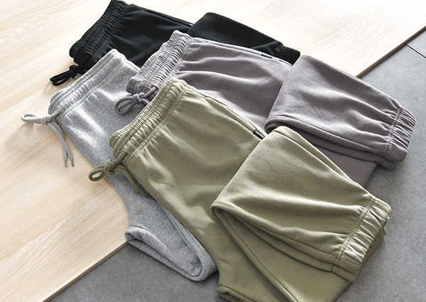 Folded jogger sweatpants in black, gray, sage, and taupe with elastic waistbands.