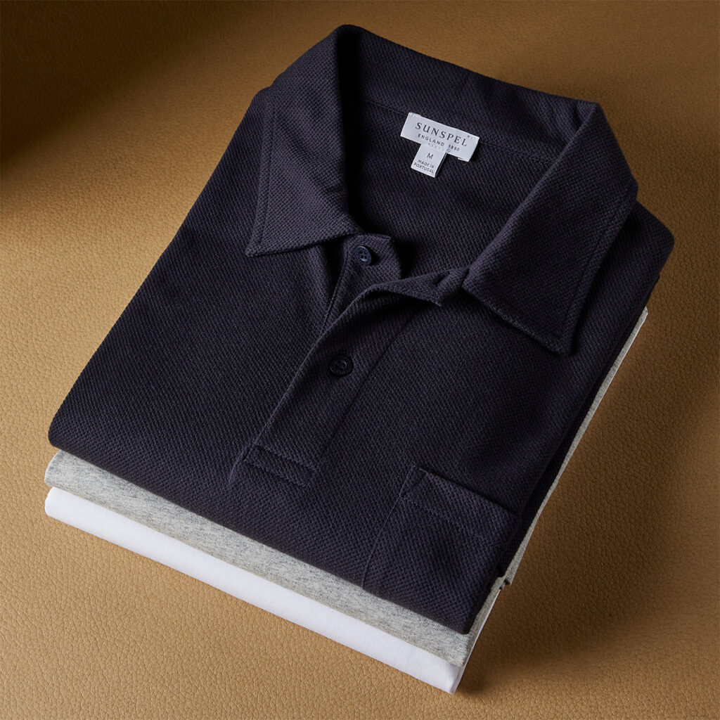 Folded navy polo shirt layered over gray and white shirts on leather surface.