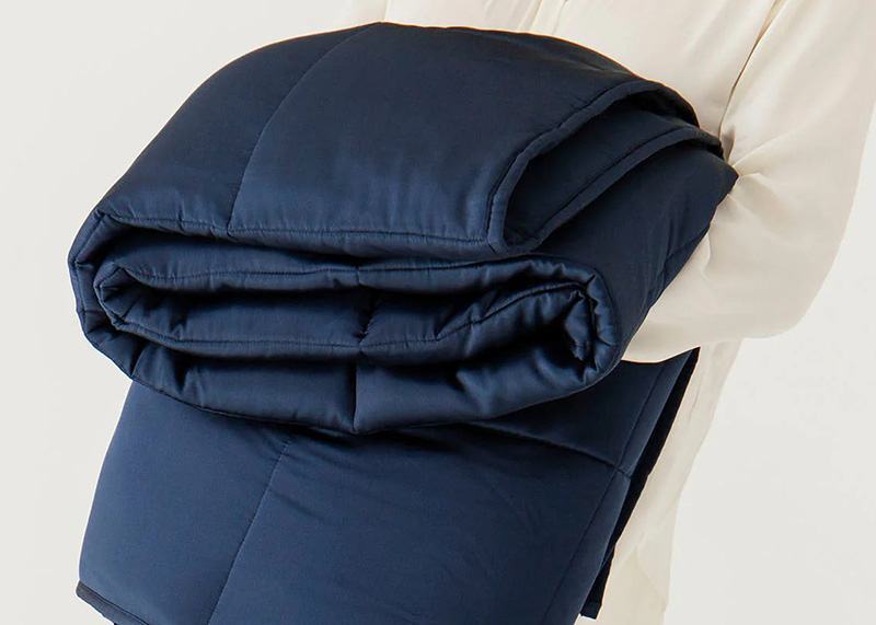 Person holding a folded navy weighted quilted blanket or padded fabric with stitched sections.