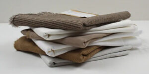 Stacked neutral-toned clothing pieces folded neatly with soft knit and cotton textures