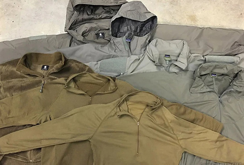 A variety of gray and olive outerwear jackets and pullovers laid out, showing different textures and zipper styles.