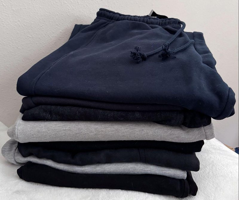Stack of folded sweatpants in navy, black, and gray on a white surface.