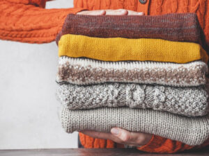 Person holding stack of colorful folded knit sweaters with textured wool fabric designs