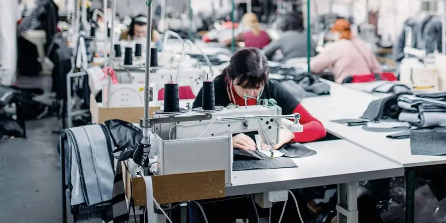 Textile factory workers sewing garments on industrial machines in busy workshop