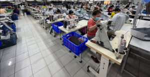Workers stitching garments in a large, busy factory floor.