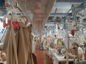 Large clothing sewing workshop with hanging fabric pieces and industrial garment production machines lined across factory floor