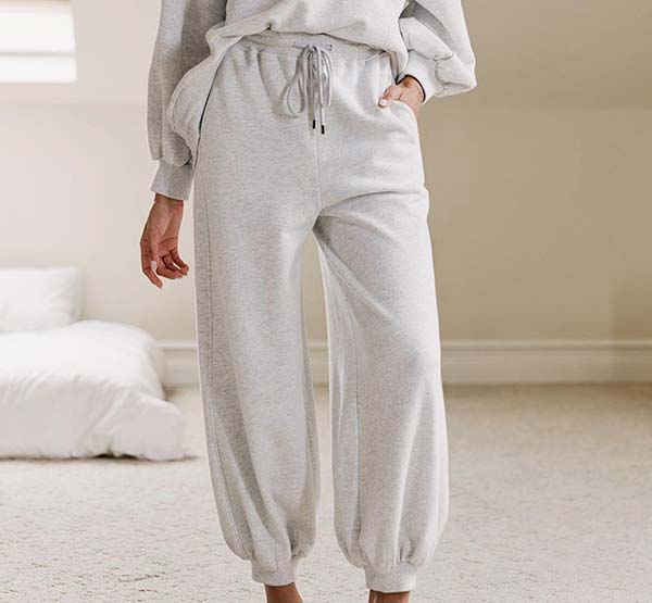 Person wearing light grey sweatpants with elastic cuffs and drawstring waist, standing indoors.