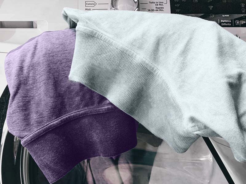 Two folded sweatshirts, one light green and one purple, placed on top of a washing machine.