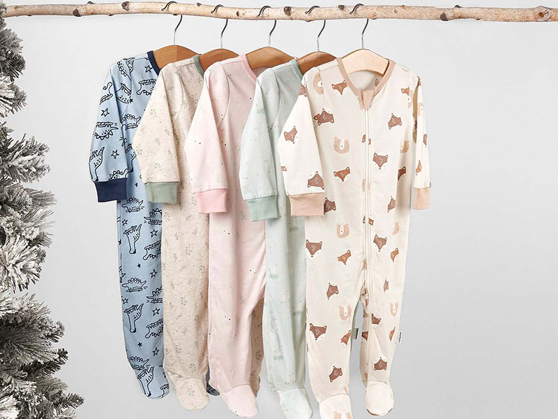 Soft pastel baby onesies with playful prints hanging on wooden hangers