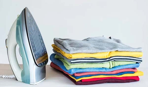 A stack of neatly folded colorful clothes next to a standing iron on a flat surface.