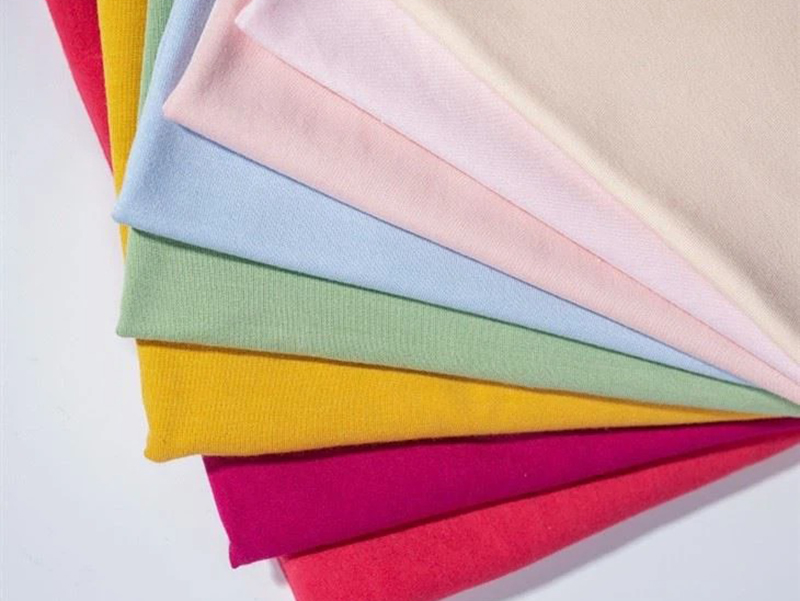 A fan arrangement of colorful fabric swatches in shades of red, pink, beige, light blue, green, yellow, and magenta, showing smooth texture and soft drape.