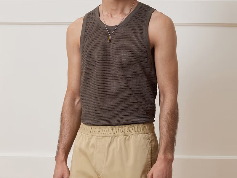 Man wearing a dark brown sleeveless mesh tank top tucked into beige elastic-waist pants.