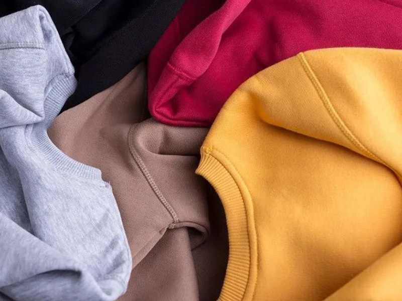 Assorted sweatshirts in gray, black, taupe, pink, and mustard layered together.