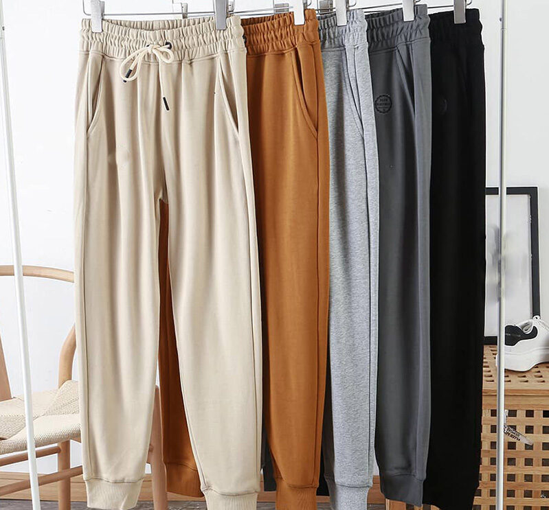 Jogger sweatpants hanging on rack in cream, mustard, gray, charcoal, and black colors.