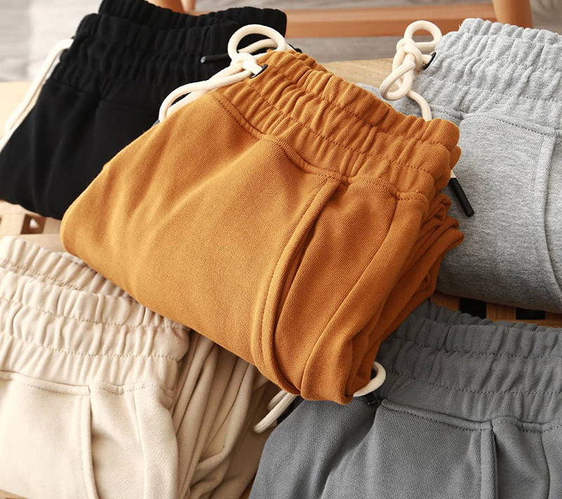 Folded jogger sweatpants in mustard, gray, cream, and black with drawstring waistbands.