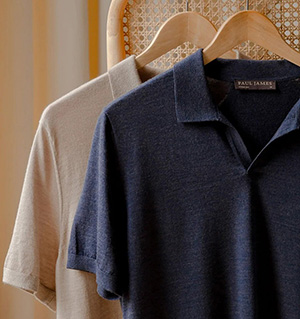 Two knit polo shirts hanging on wooden hangers in cream and navy colors.